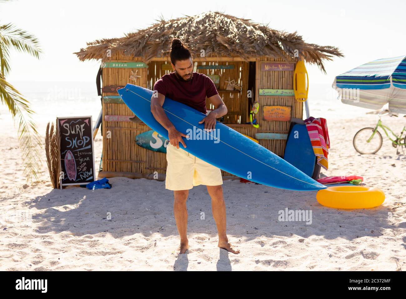 Uomo da corsa misto che tiene il surf board sulla spiaggia Foto Stock