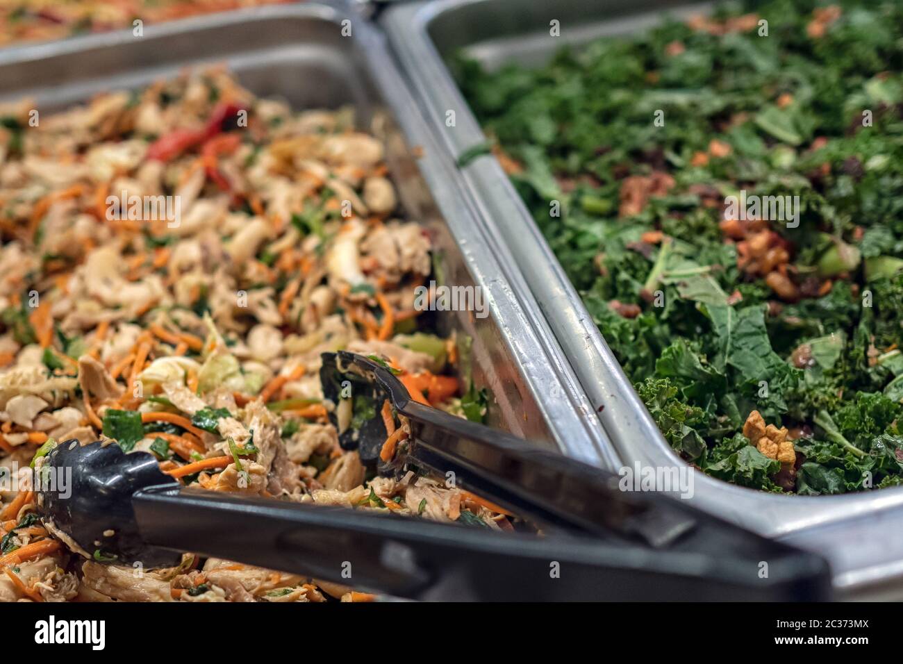 Insalata fresca in vassoi presso un Deli self-service con pinze di servizio Foto Stock