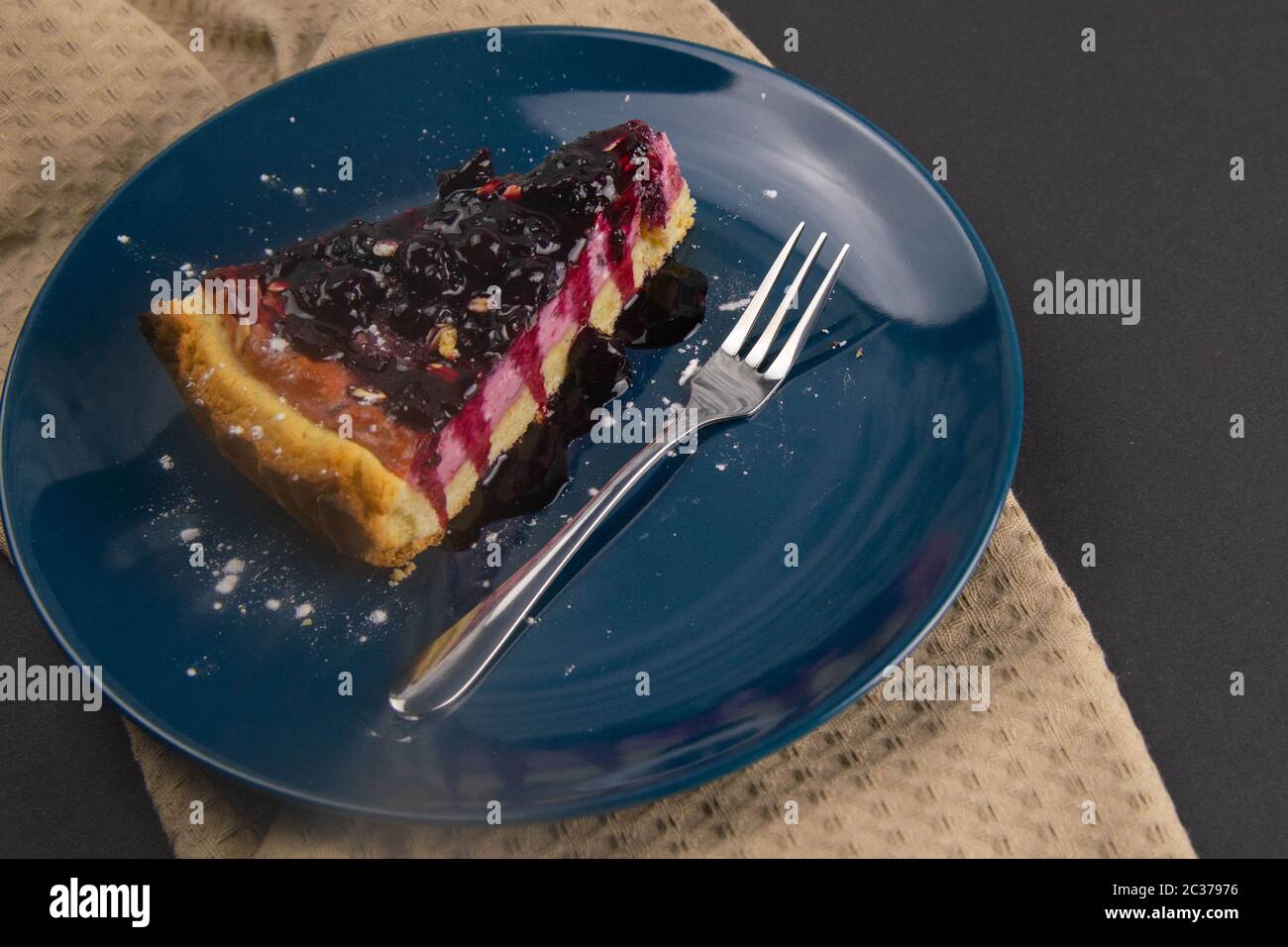 Fette di torta mousse di mirtillo con riflessi frutti di bosco decorati e foglie di menta su una piastra blu sono su tavola nera, primo piano. Viste dall'alto. Foto Stock