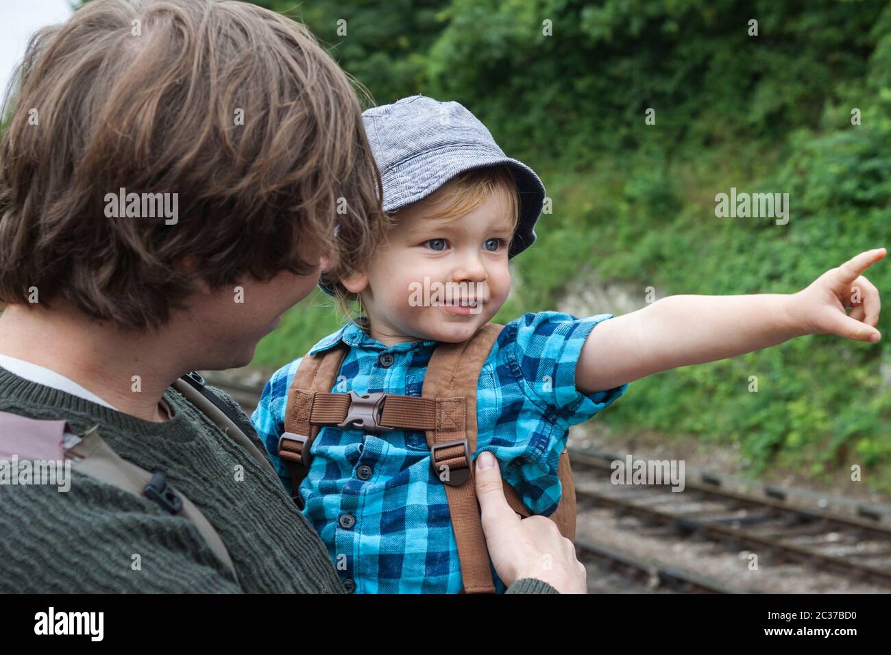 Padre e figlio (2 anni) alla stazione di Alresford sulla Mid-Hants Railway, Hampshire, Inghilterra, Regno Unito. Ragazzo eccitato che punta a un treno Foto Stock