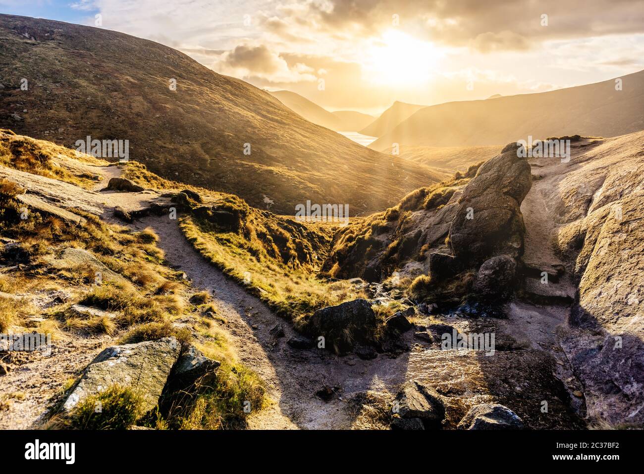 Sentiero e grande masso che conduce alla valle con serbatoio d'acqua, tramonto spettacolare con raggi di sole. MOU Foto Stock