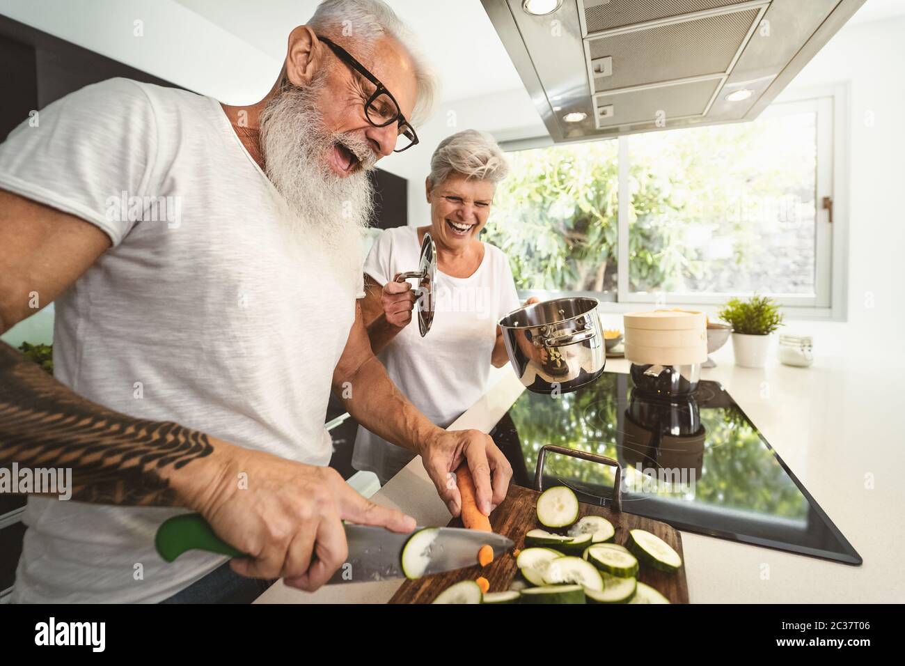 Felice coppia anziana che si diverte a cucinare insieme a casa - anziani che preparano un pranzo di salute in cucina moderna Foto Stock