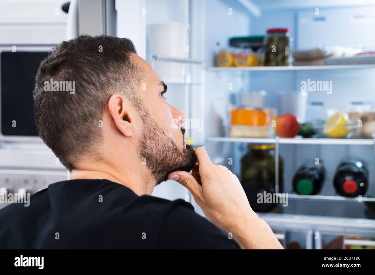 Affamato uomo confuso guardando in Open Frigo in cucina Foto Stock
