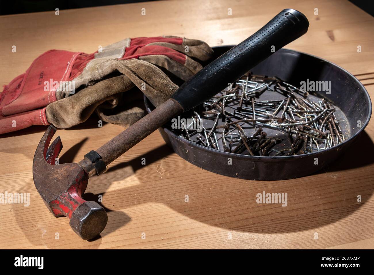 Vecchio arrugginito martello e guanti di costruzione prevista sul pannello di legno in studio Foto Stock