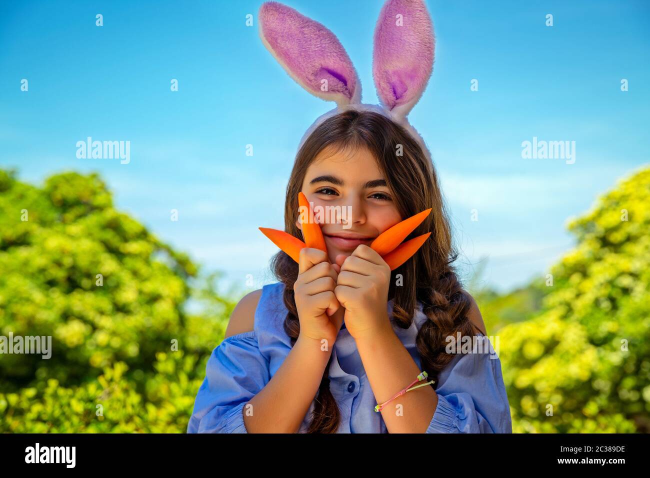 Ritratto di una bambina carina vestita da coniglietto che gioca con carote, giardinaggio e divertirsi all'aperto nel giorno di primavera soleggiato, festa di Pasqua outdoo Foto Stock