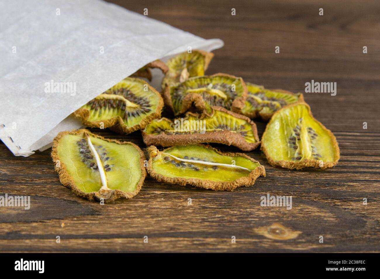 Una foto di Kiwi essiccato caduto da una borsa di carta kraft su una struttura di legno scuro. Foto Stock