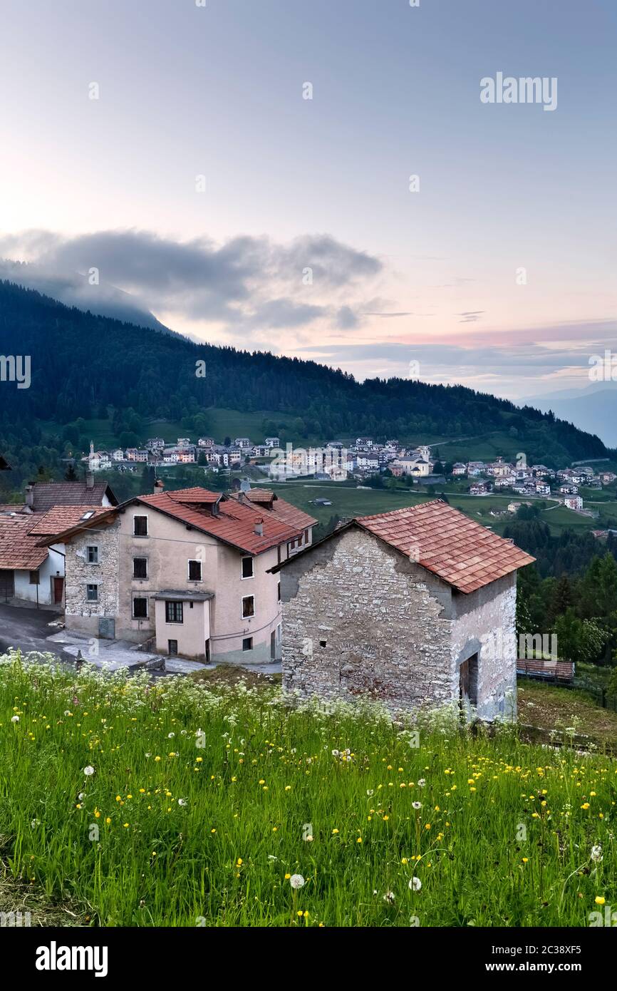 La notte cade al villaggio di Perpruneri sull'Alpe Cimbra. Sullo sfondo il paese di San Sebastiano. Folgaria, Trentino, Italia. Foto Stock