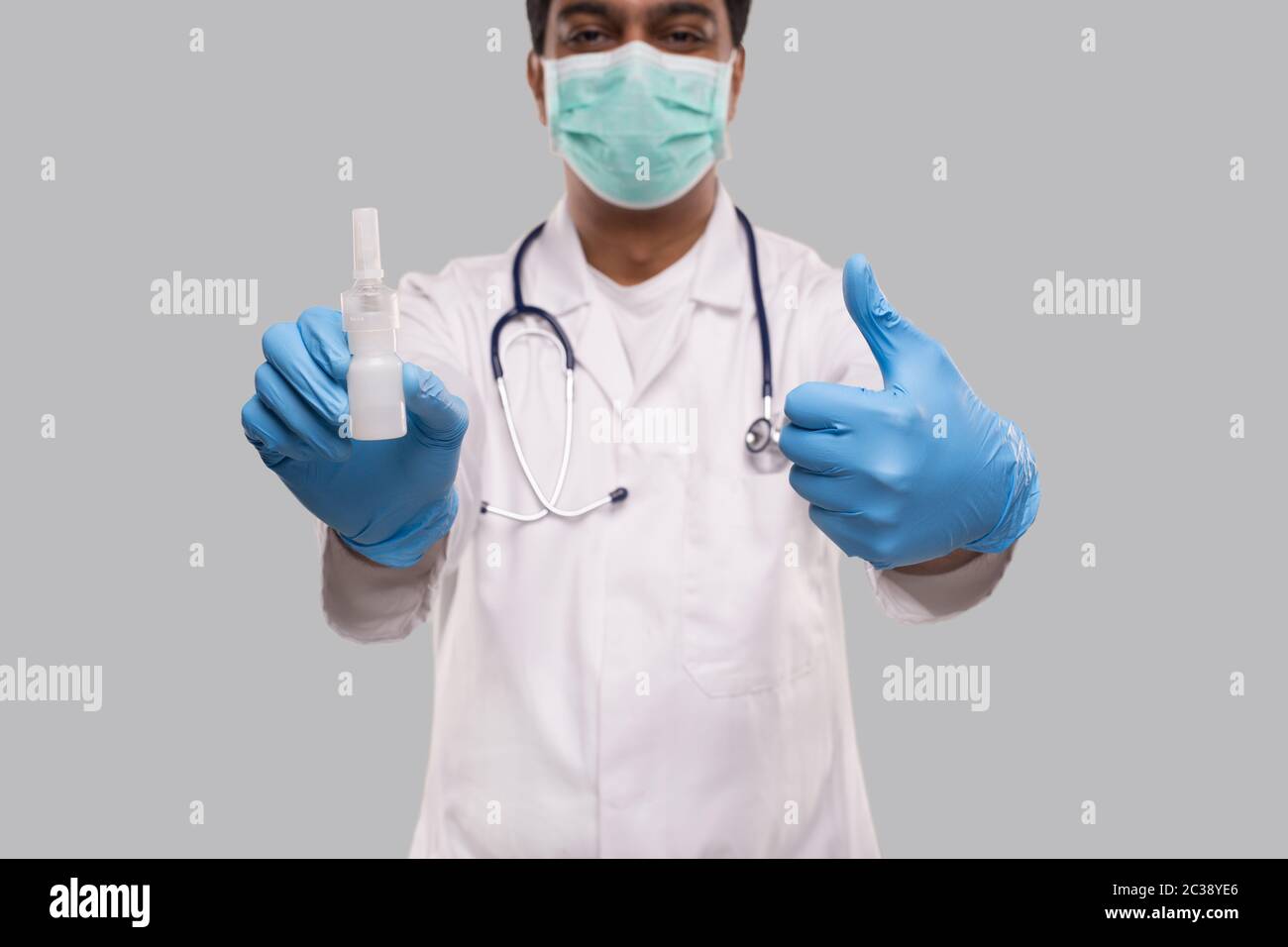 Medico che mostra spray al naso e pollice su indossare maschera medica e guanti primo piano. L'uomo indiano medico spray nasale. Concetto di virus corona. Isolato Foto Stock