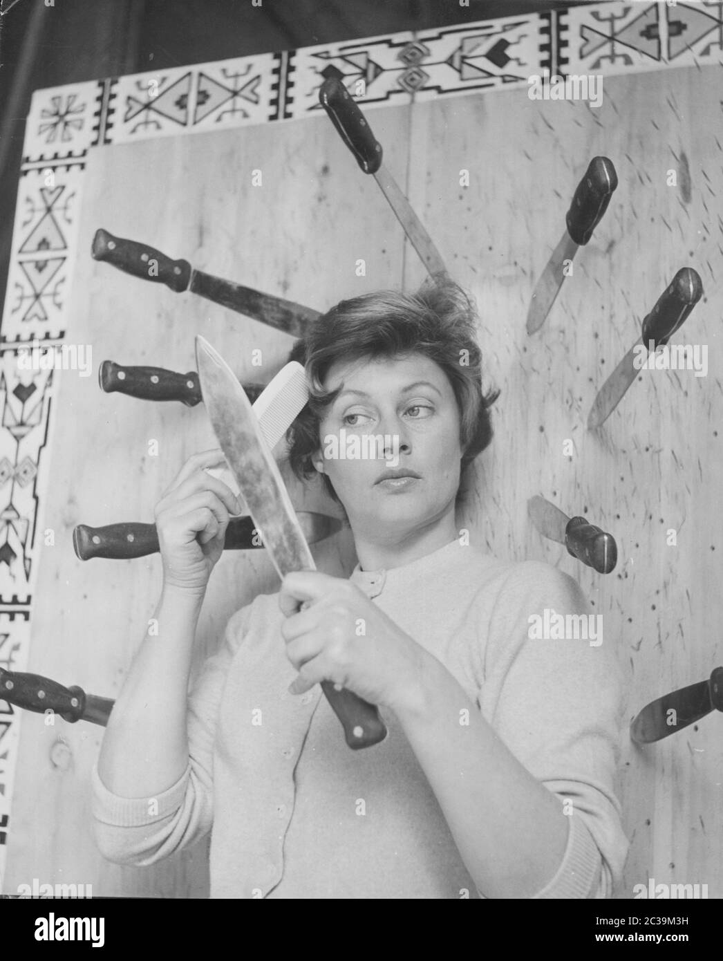 L'assistente di un lanciacoltelli rimane impresso nel mezzo dei coltelli, usa una lama come specchio e dispone il suo capelli (colpo non fatto). Foto Stock
