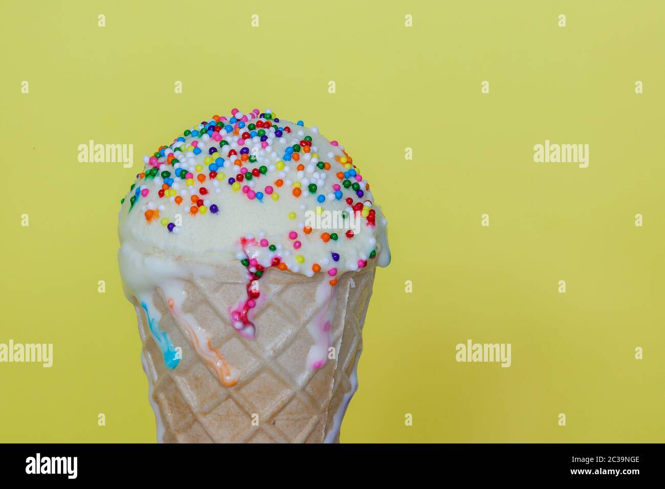 Gelato alla vaniglia con poco arcobaleno spruzzare in un cono di cialda e sfondo giallo Foto Stock