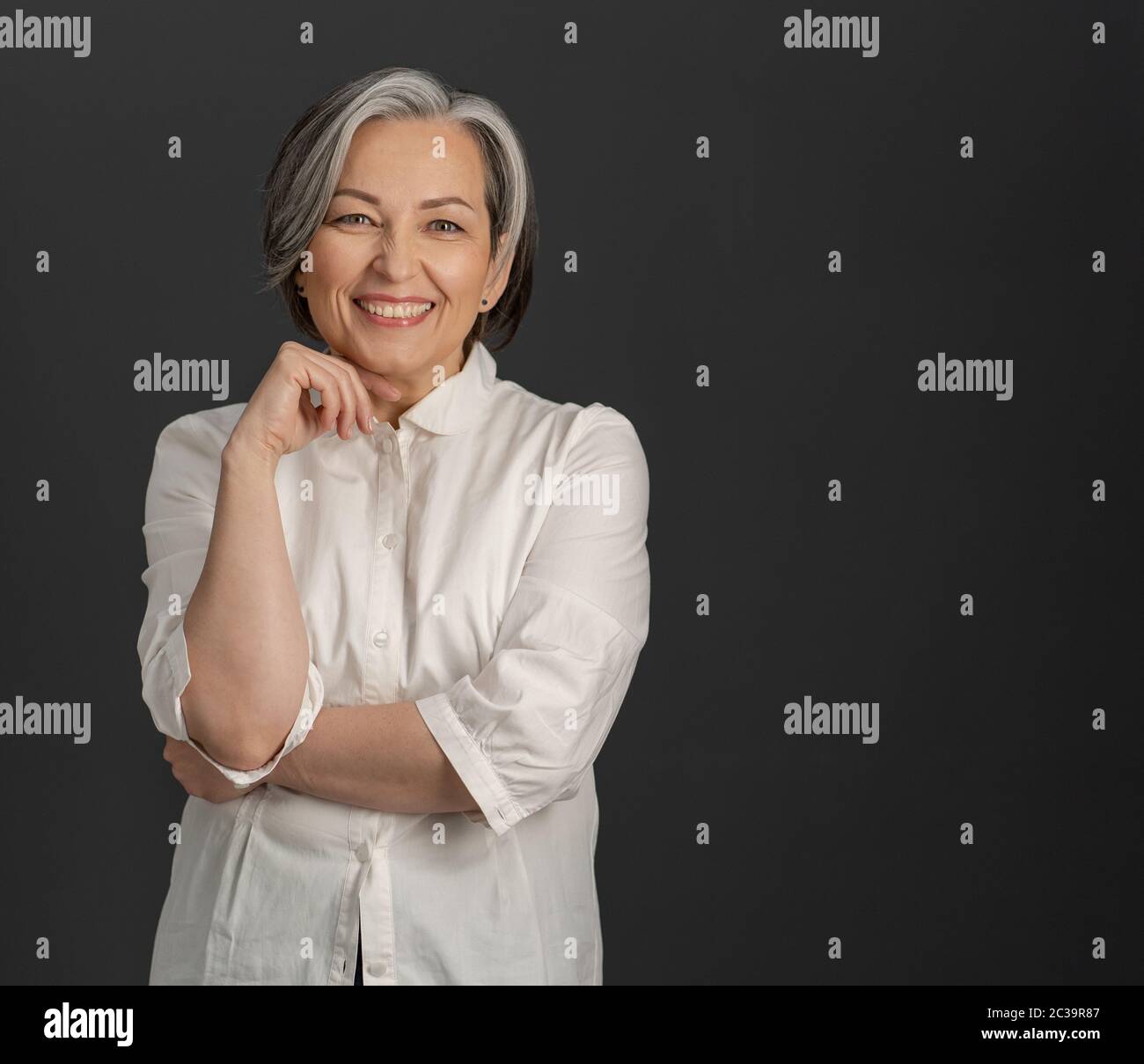 Felice uomo d'affari con capelli grigi sorride alla macchina fotografica. Bella donna in camicia di frusta che posa su sfondo grigio con spazio di testo a destra Foto Stock