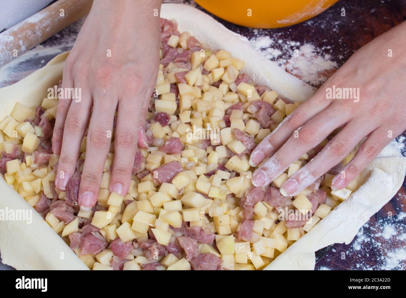 Cottura con torta di patate e carne. Le mani delle donne lay out tagliare le patate e i pezzi di carne con l'impasto arrotolato giacente sul tavolo. Foto Stock