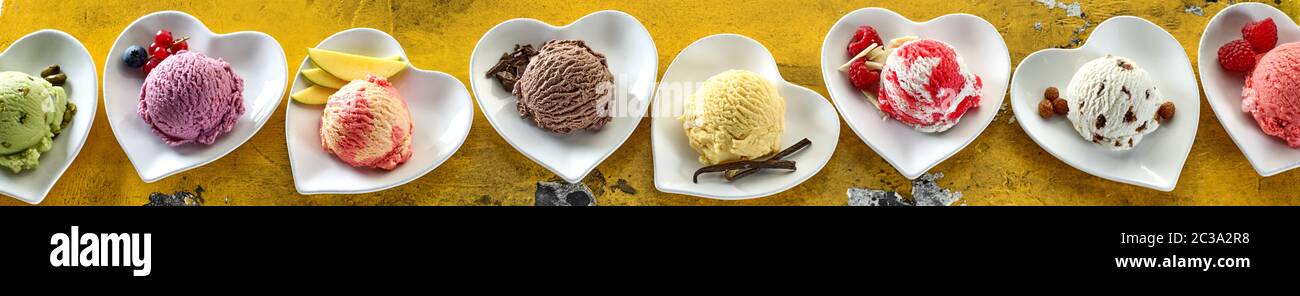 Ampio panorama banner con gusti assortiti di gelato servito in scoop su a forma di cuore ad ciotole con ingredienti freschi per una testata o pubblicità Foto Stock