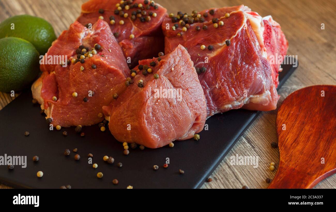 La carne rossa su una lavagna nera cosparsi di pepe, aglio, anice e calce. Billette per barbecue, bistecca o shish kebab. La cottura per il pranzo la matrice fresca Foto Stock