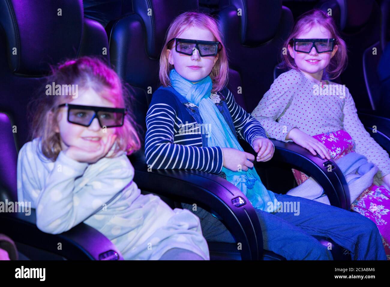 Tre bambini bambini ragazze bambini bambini bambine ragazze / sorelle seduti in comode sedie interattive cinema posti in un cinema tridimensionale 3-D / 3 D /, con occhiali speciali occhiali da vista. UK (117) Foto Stock