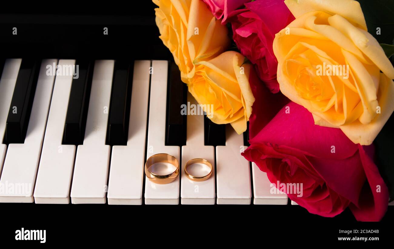 Mazzo di rose giacente sul piano con gli anelli di nozze. Giallo e rose rosse regalo di nozze con le fedi. Preparazione per un matrimonio o di San Valentino d Foto Stock