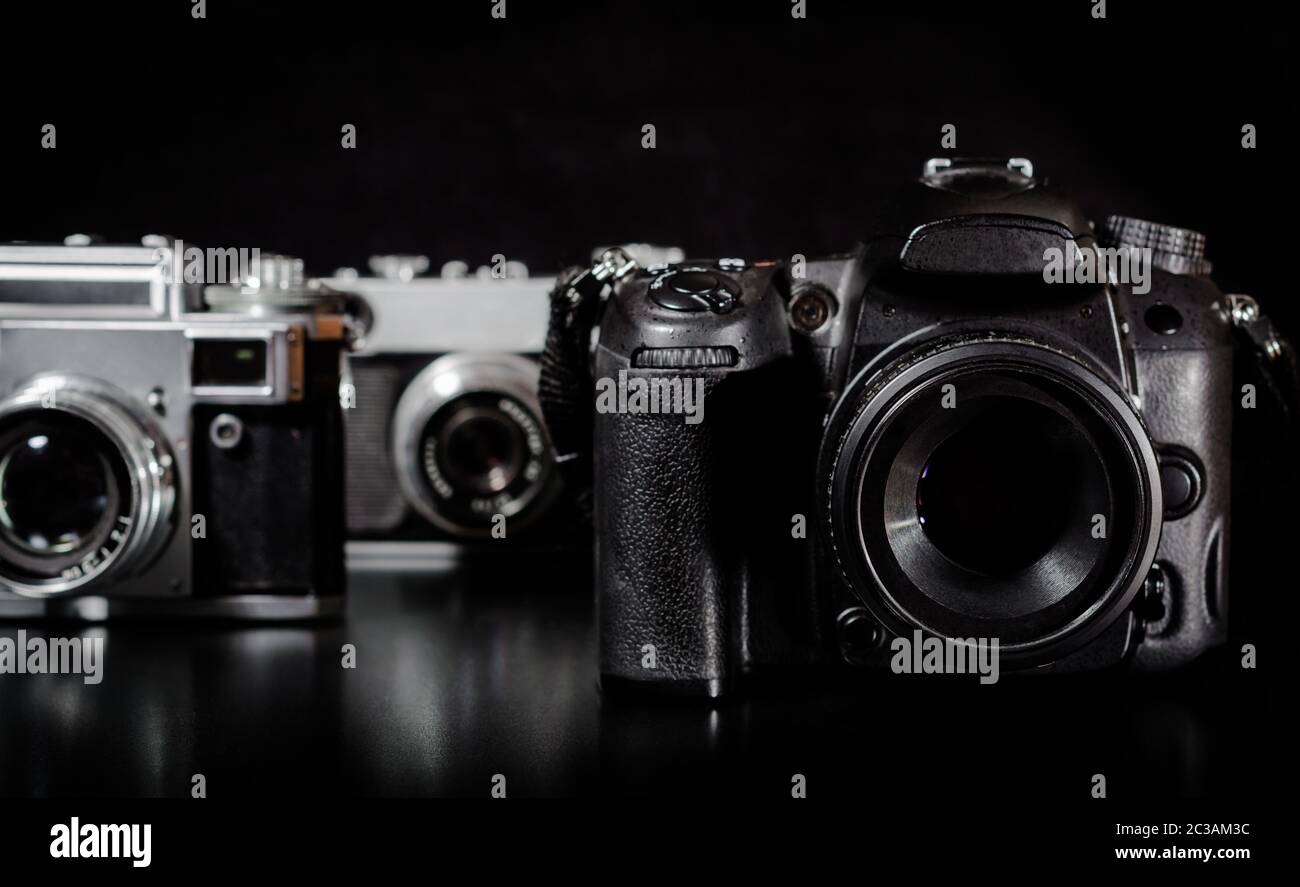 Due fotocamere vintage e una moderna fotocamera su uno sfondo nero in primo piano Foto Stock