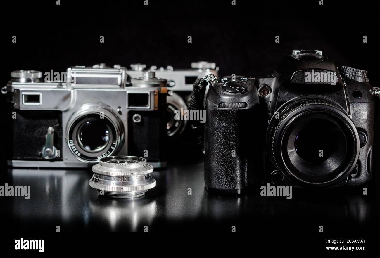 Due macchine fotografiche d'epoca con la lente e una moderna fotocamera su uno sfondo nero in primo piano Foto Stock
