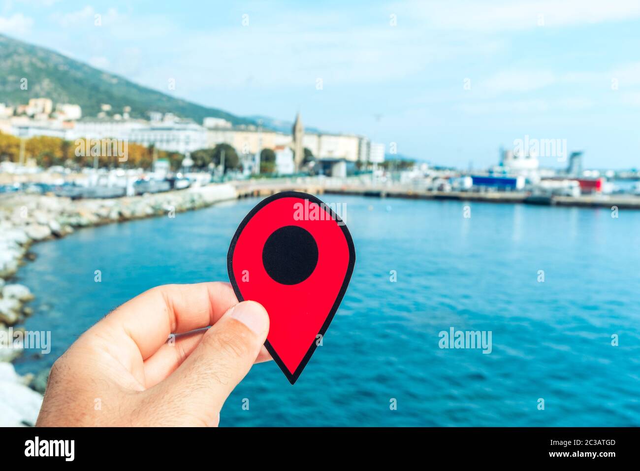 La mano di un giovane caucasico con un pennarello rosso che punta al porto di Bastia, in Corsica, Francia, con il porto commerciale a destra e il non Foto Stock