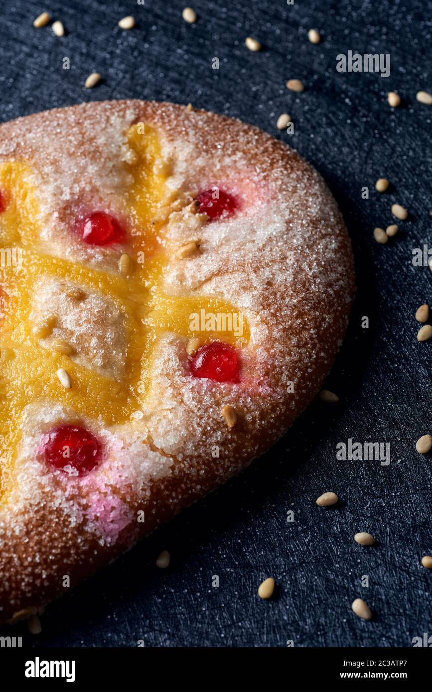 Primo piano di una coca de Sant Joan, una tipica dolce torta piatta della Catalogna, Spagna, mangiata a San Giovanni, su una superficie di tessuto nero cosparsa di pi Foto Stock