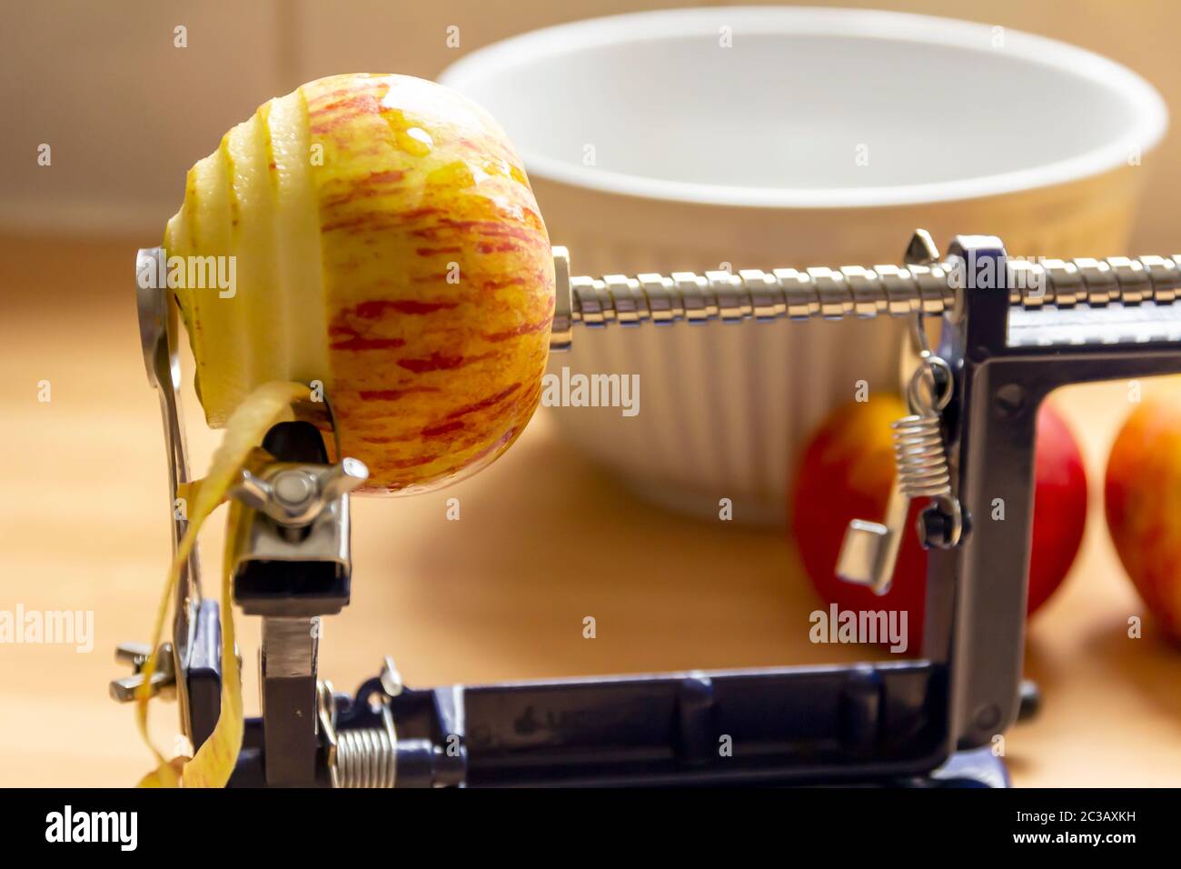 Una mela sbucciata con un pelatore meccanico di mele, con una ciotola e più mele sullo sfondo Foto Stock