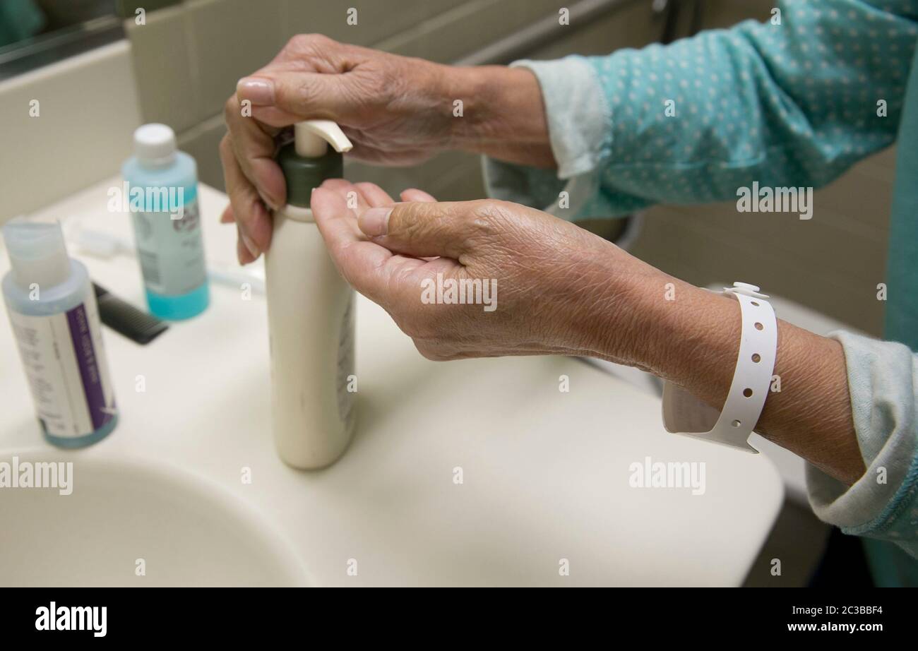 Austin Texas USA, febbraio 11 2014: Donna ispanica di 75 anni, indossando un bracciale di plastica per l'ospedale per dimostrare che è una paziente, si tira la lozione sulla sua mano nella sua stanza d'ospedale. ©Marjorie Kamys Cotera/Daemmrich Photography Foto Stock