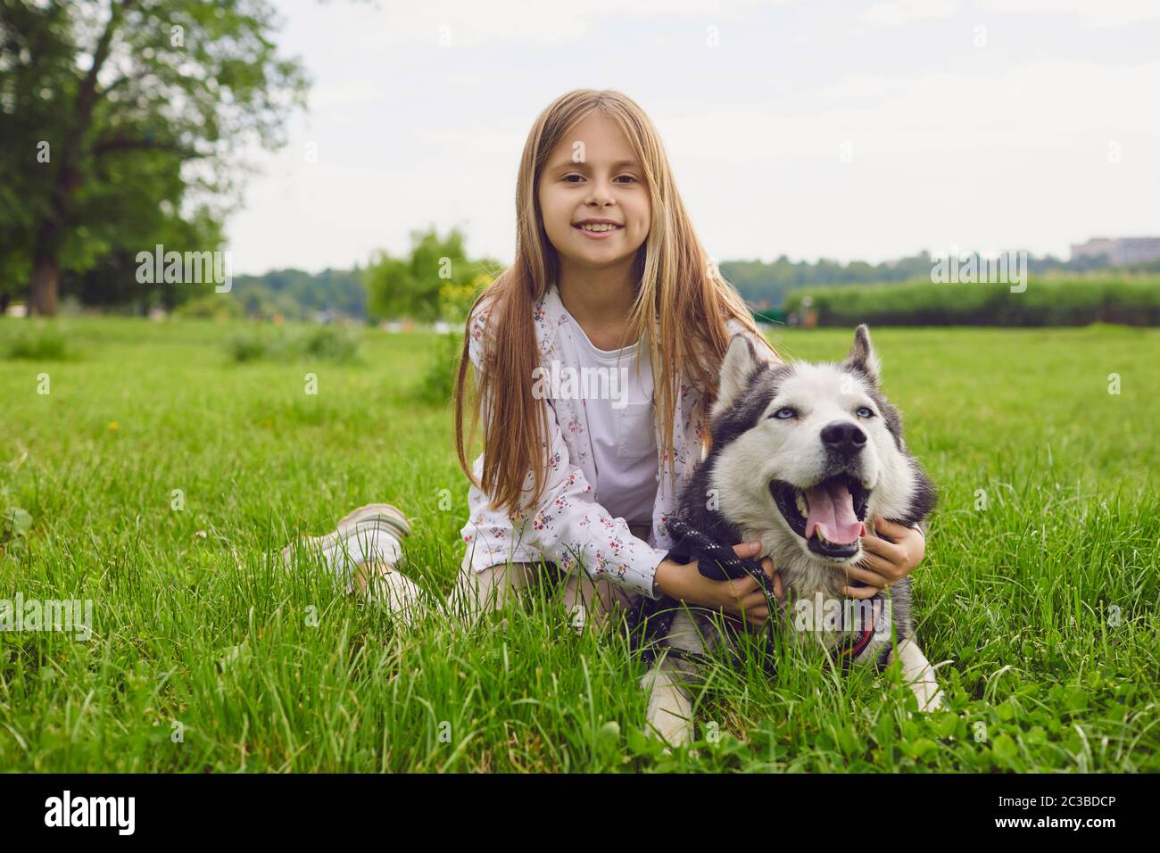 Sorridente bambino con un cane da compagnia, il cane Husky gioca su un prato in estate in primavera nel parco. Foto Stock