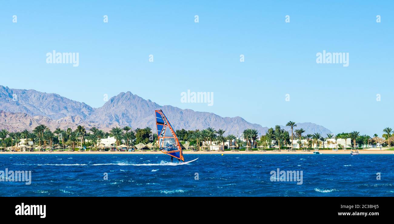 windsurf corre sul mare sullo sfondo della spiaggia con palme e alte montagne rocciose Foto Stock