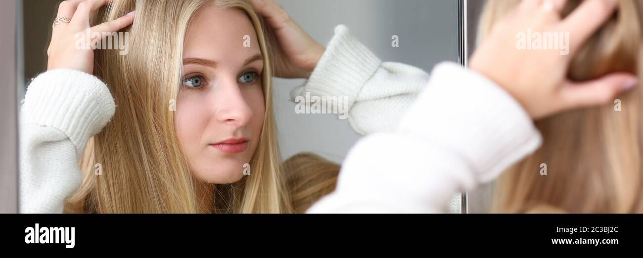 La ragazza guarda il riflesso, raddrizza i capelli Foto Stock