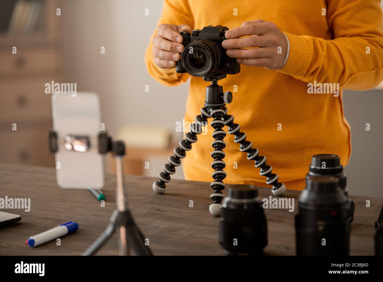Mani di fotografo professionista che fissa la fotocamera sul treppiede davanti allo smartphone mentre fanno lezione per il pubblico online Foto Stock