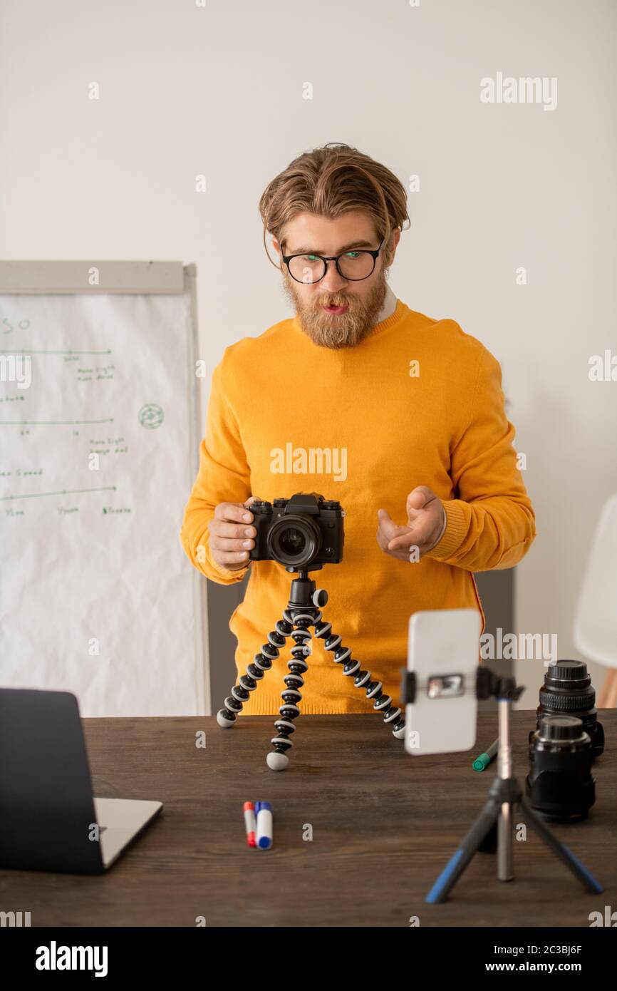Giovane insegnante di fotografia professionale che mostra un nuovo modello di fotocamera ai suoi studenti online e ne spiega le caratteristiche Foto Stock