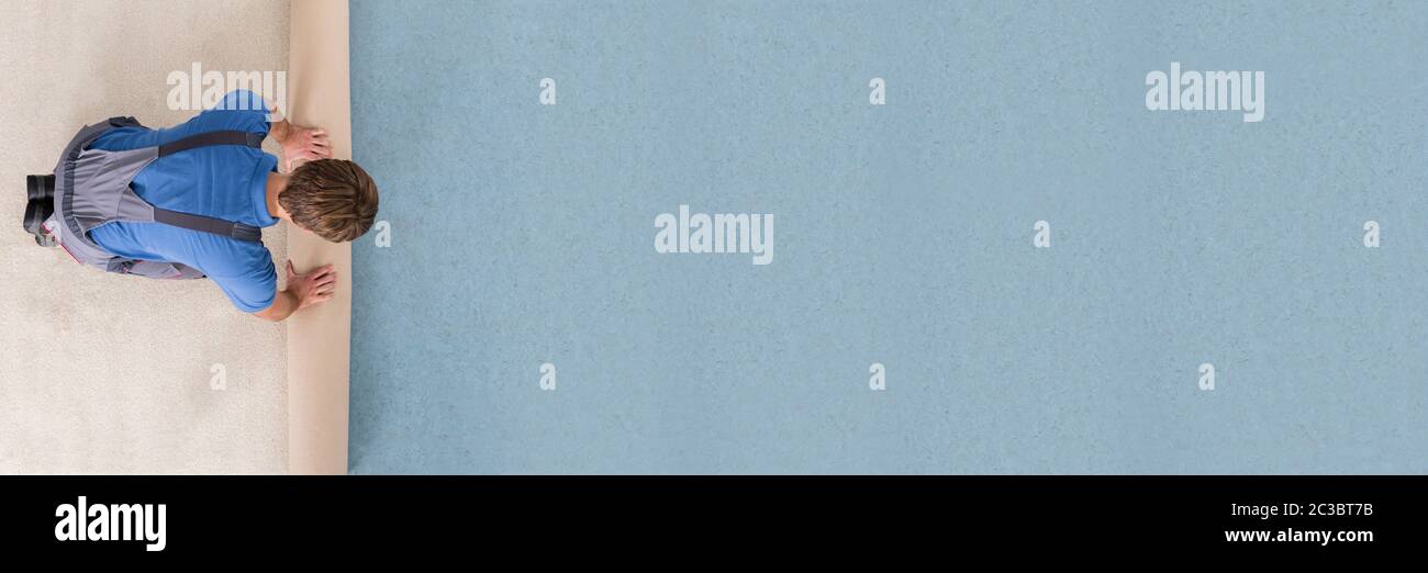 Angolo di Alta Vista del lavoratore in uniforme svolgimento tappeto sul pavimento Foto Stock