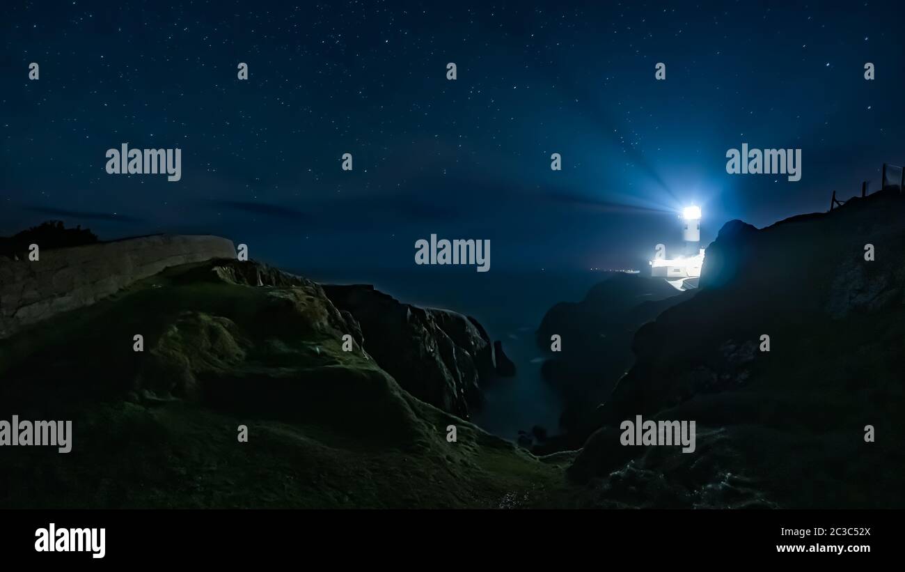 Raggi di luce che brillano dal faro di Fanad Head nella notte buia con cielo pieno di stelle Foto Stock