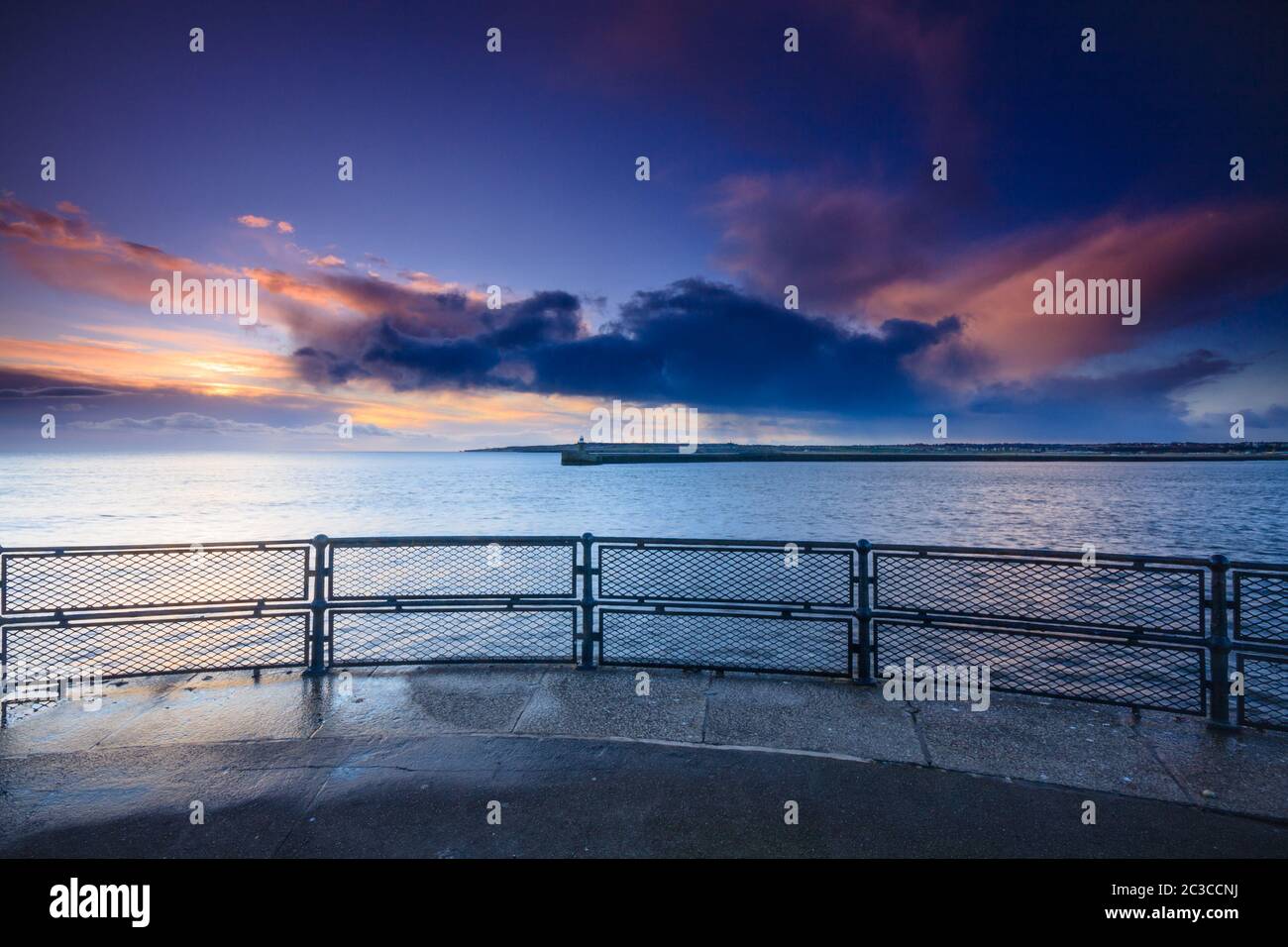 Un'alba d'inverno sul molo di Tynemouth, che guarda fuori sopra le ringhiere attraverso il porto sul mare del nord e la luce del sole che sorge sulle nuvole Foto Stock
