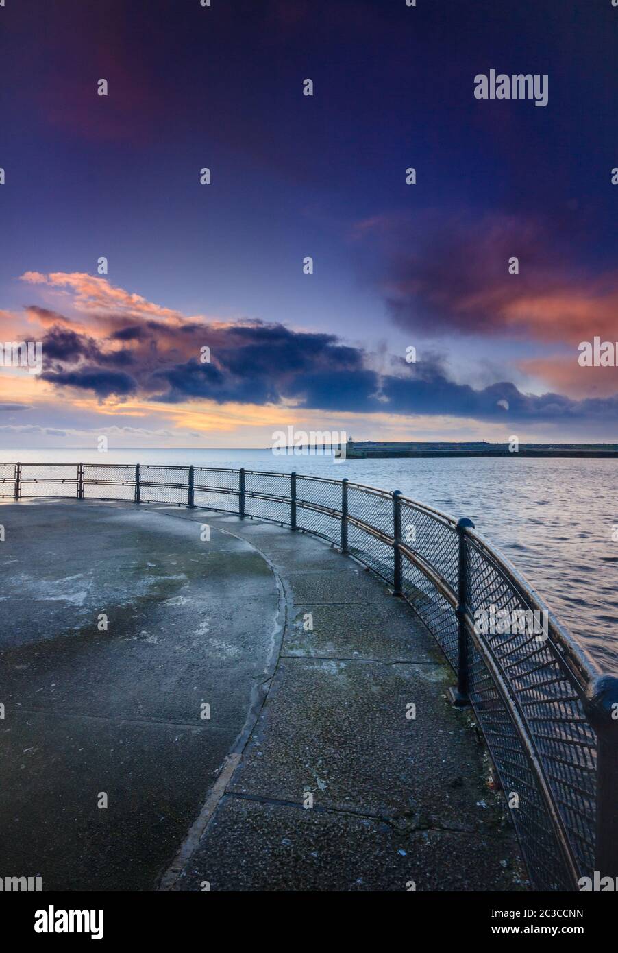Un'alba d'inverno sul molo di Tynemouth, che guarda fuori sopra le ringhiere attraverso il porto sul mare del nord e la luce del sole che sorge sulle nuvole Foto Stock