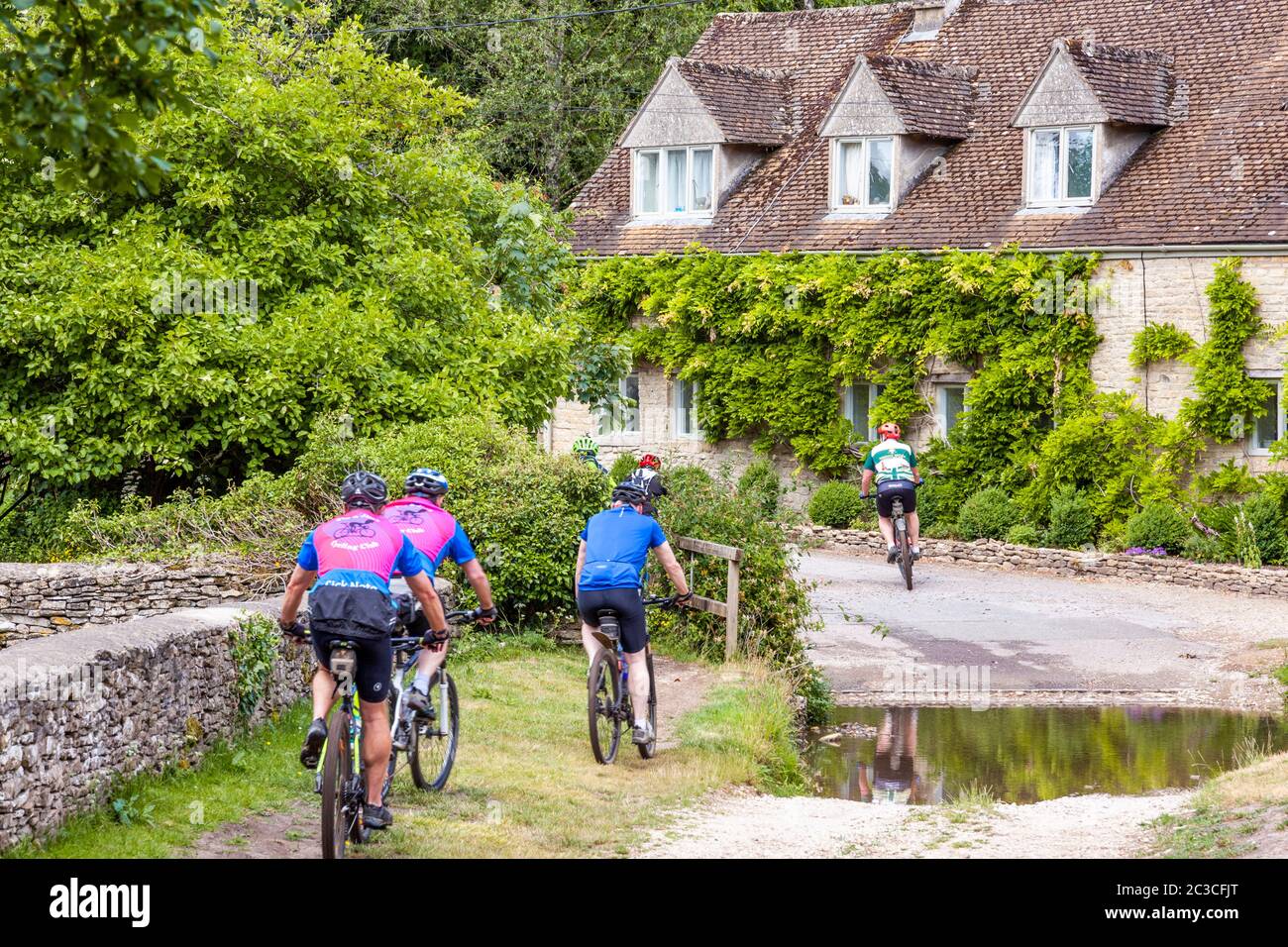 Ciclisti passando case accanto al ford nel villaggio di Cotswold di Duntisbourne Rouse, Gloucestershire Regno Unito Foto Stock