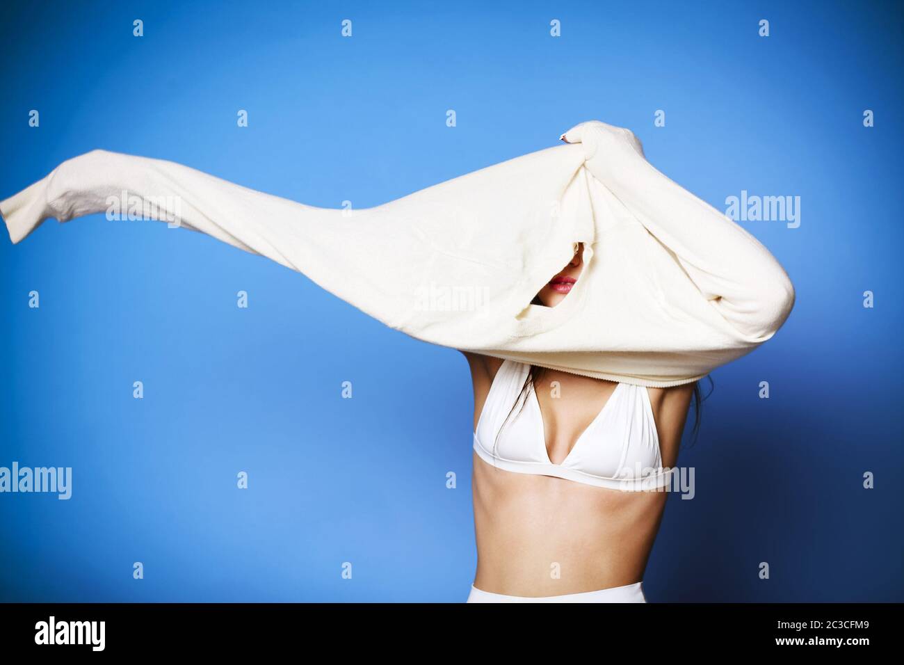 Felice giovane femmina sorridente e decollo morbido e caldo maglione su sfondo blu Foto Stock