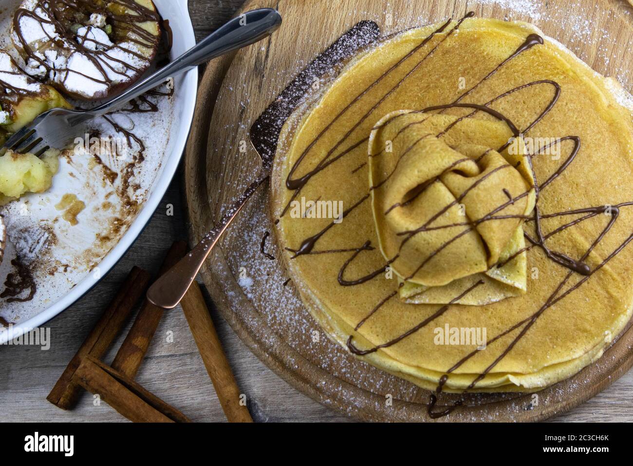 Mele caramellate con miele e cannella in una ciotola di argilla e frittelle con burro e cioccolato su uno sfondo di legno chiaro. Viste dall'alto Foto Stock