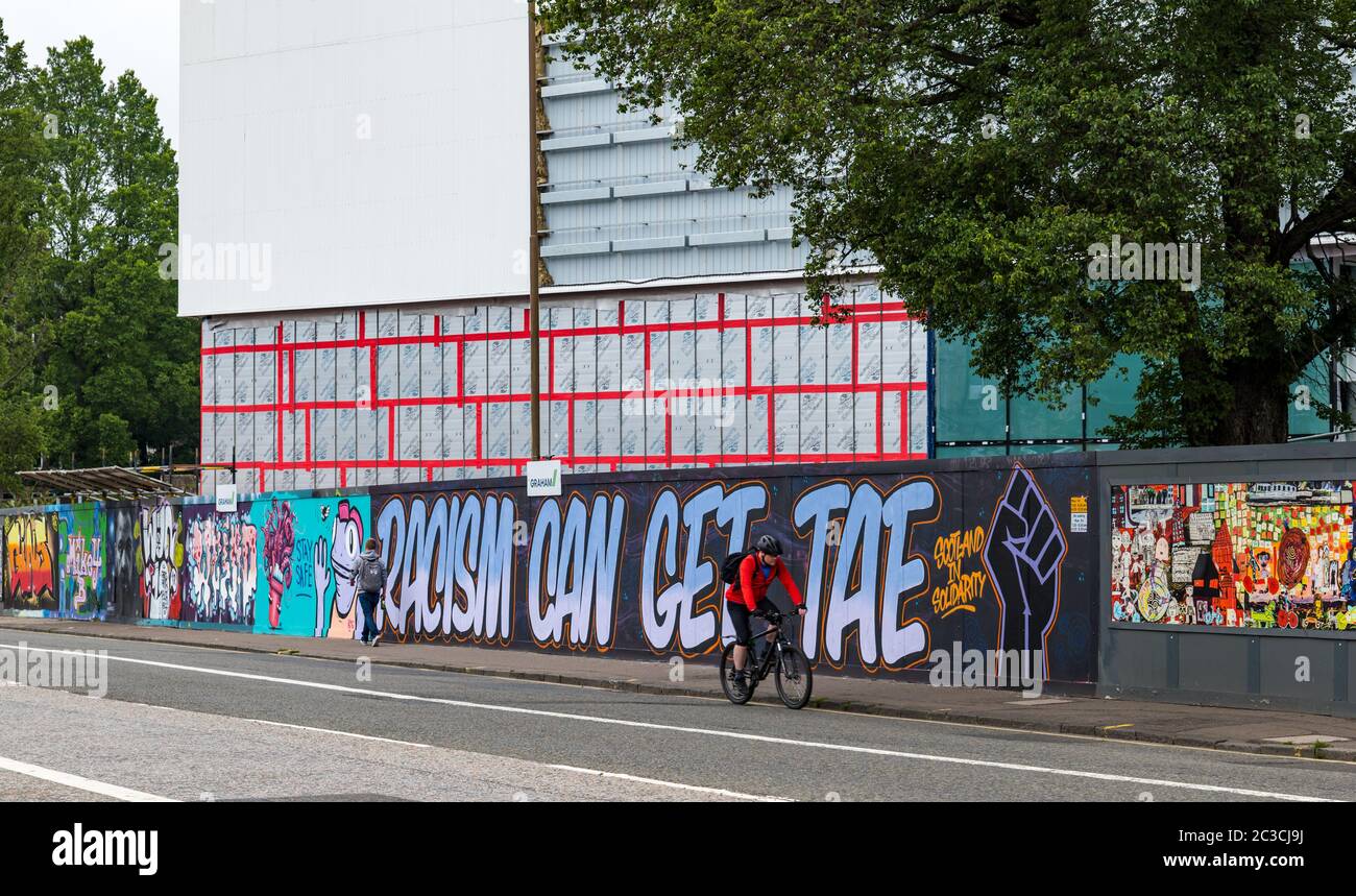 Edimburgo, Scozia, Regno Unito, 19 giugno 2020. Black Lives Matter Mural Trail: Un nuovo percorso di opere d'arte si sta sviluppando presso i luoghi per supportare la campagna BLM avviata dal produttore artistico Wezi Mhura. Nella foto: Graffiti BLM del collettivo Graffiti sulle corse al nuovo stadio Meadowbank in costruzione, mentre un ciclista passa in passato Foto Stock