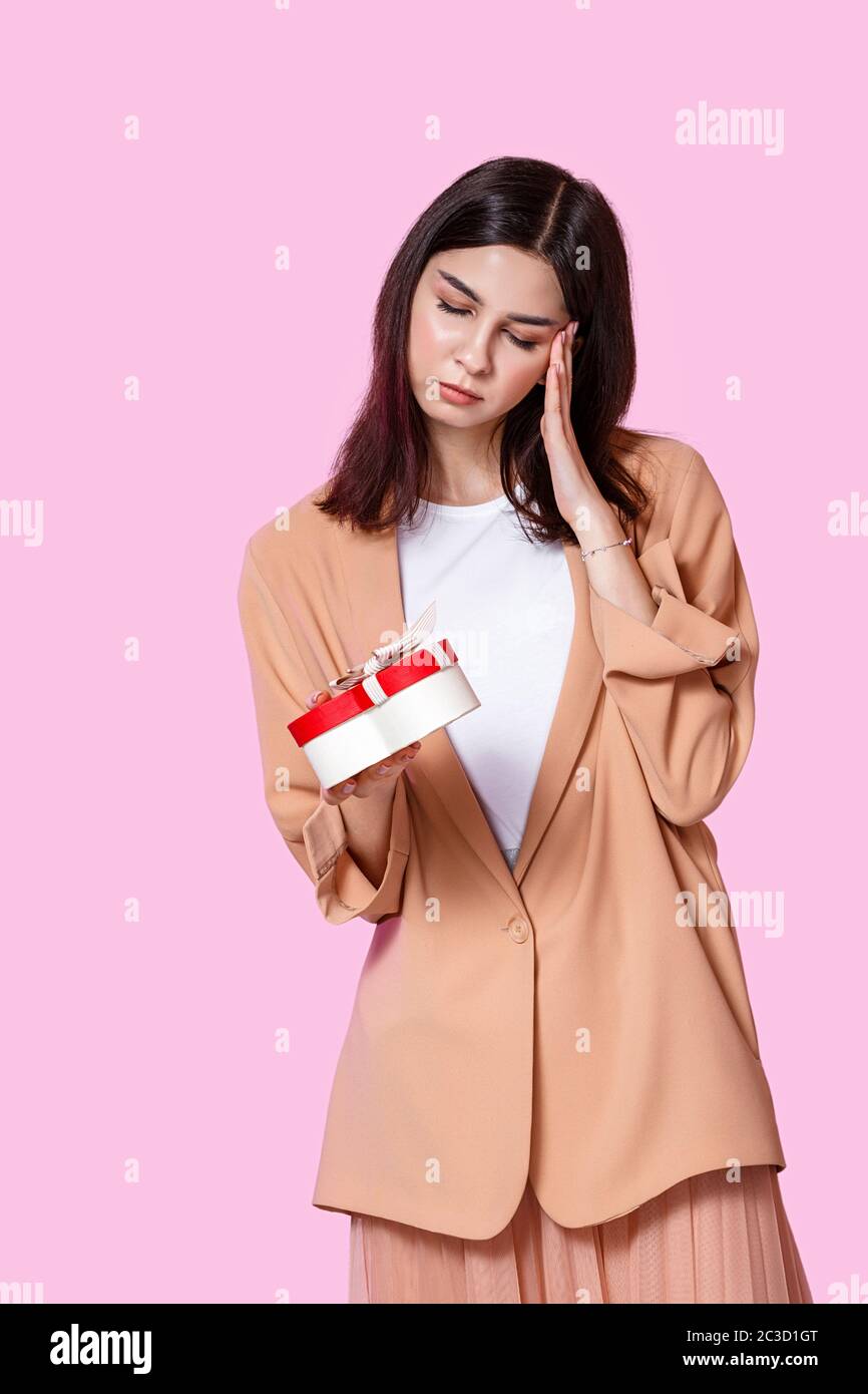 una giovane ragazza in una giacca leggera con una scatola regalo nelle sue mani. insoddisfatto e deluso . su uno sfondo isolato rosa. Foto Stock