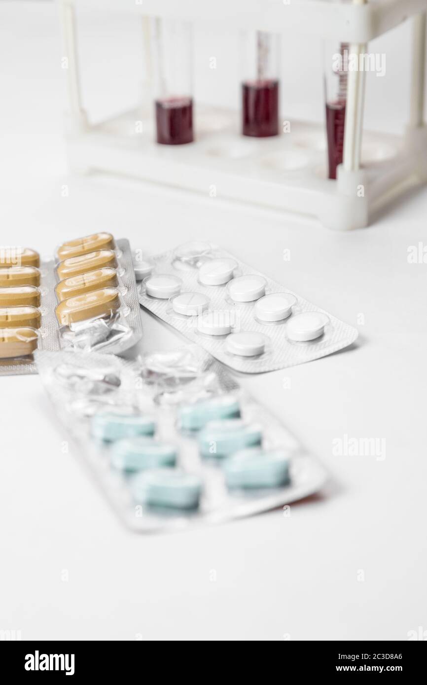 farmaci in confezioni e campioni di sangue in provette in background. su sfondo medico bianco Foto Stock