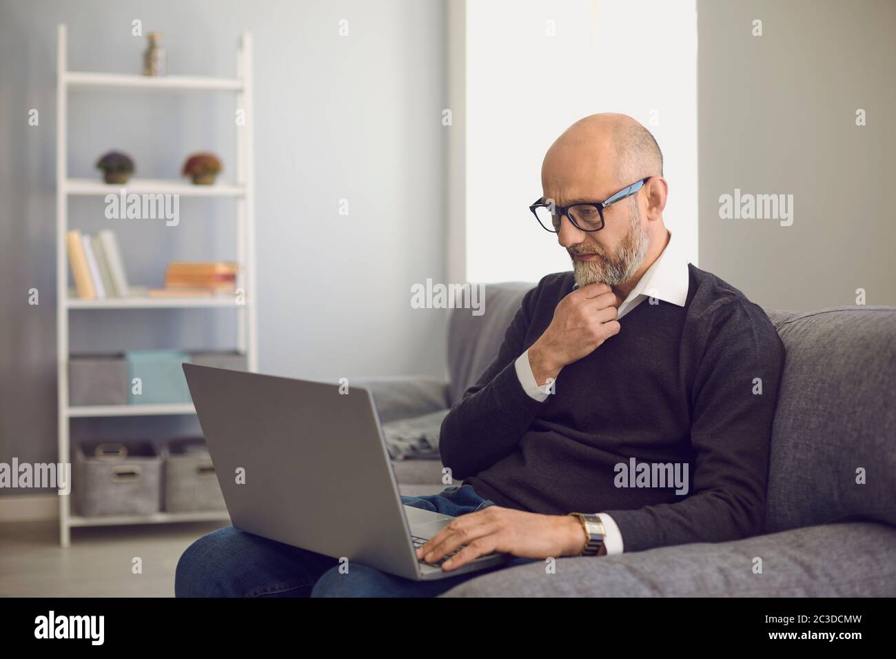 Uomo anziano con il laptop che comunica online, lavorando, consultando il medico o prendendo corso di formazione a casa Foto Stock