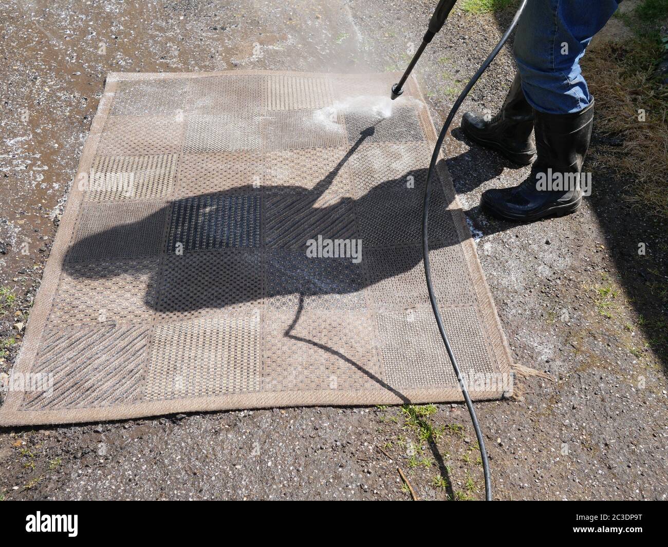 Lavaggio a pressione di un tappeto esterno, silhouette di uomo in stivali, fatto in blocco! Foto Stock