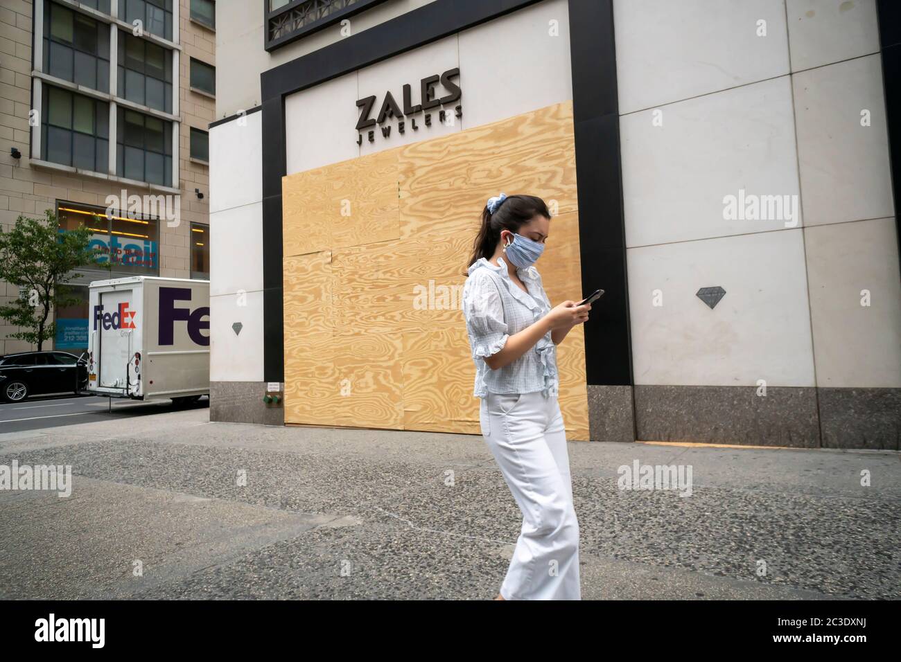 Una donna mascherata distratta dal suo smartphone passa davanti a un negozio di gioielleria Zales sulla Fifth Avenue a New York giovedì 11 giugno 2020. Signet Jewellers, il proprietario dei marchi di gioielli Zales, Kay, Piercing Pagoda e Jared ha riferito che chiuderà 380 negozi negli Stati Uniti e in Europa. (© Richard B. Levine) Foto Stock