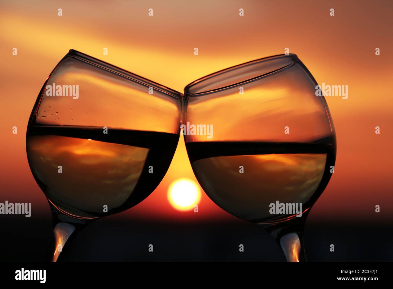 Due bicchieri con vino bianco sullo sfondo del tramonto, il sole serale si riflette in un bicchiere. Concetto di celebrazione, serata romantica, data d'amore Foto Stock