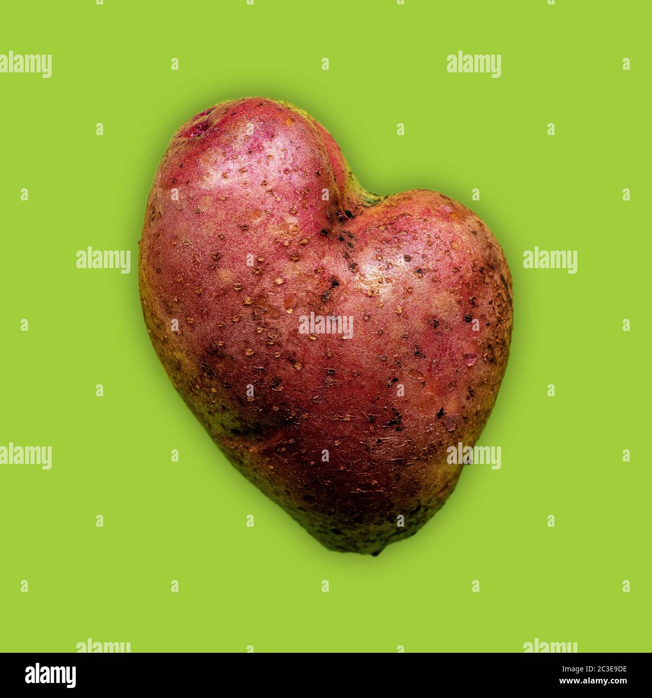 Patata a forma di cuore con buccia rossa su sfondo verde Foto Stock