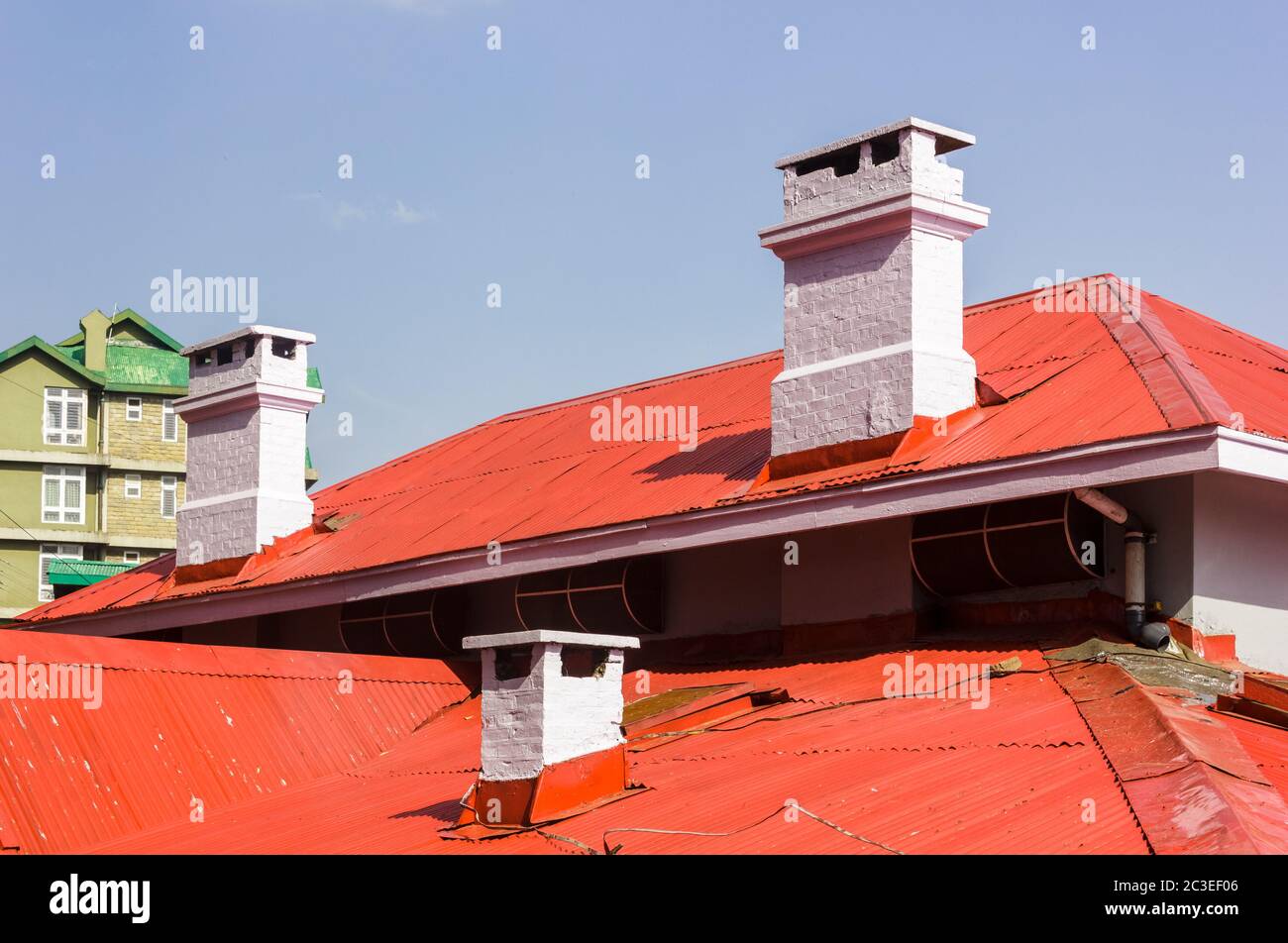 Piccoli camini bianchi sui tetti in teglia, rossi e inclinati, di una vecchia casa coloniale nella stazione collinare di Shimla in India. Foto Stock