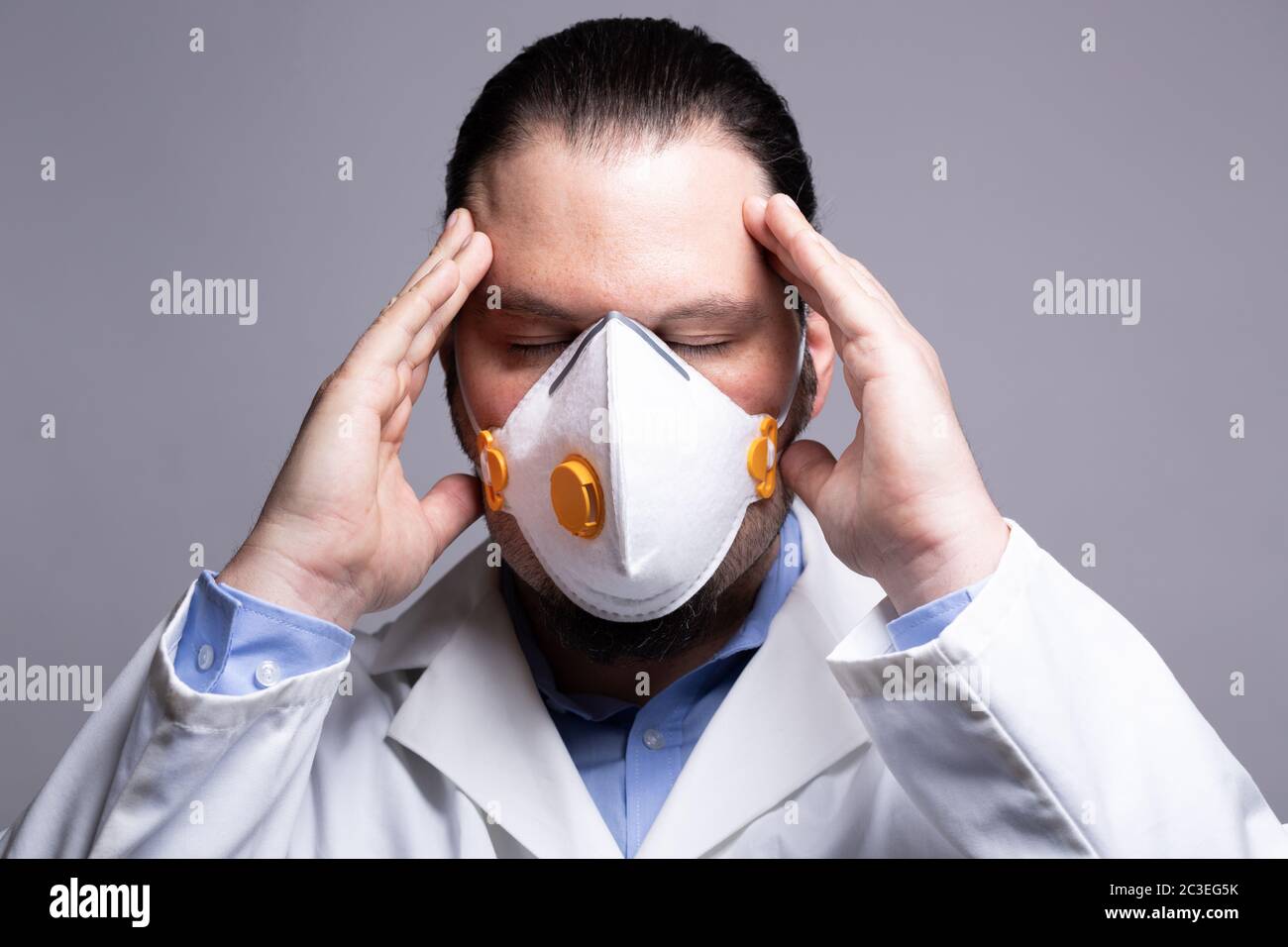Medico frustrato che indossa una maschera respiratoria che tocca la testa con le mani. Burnout e. Foto Stock