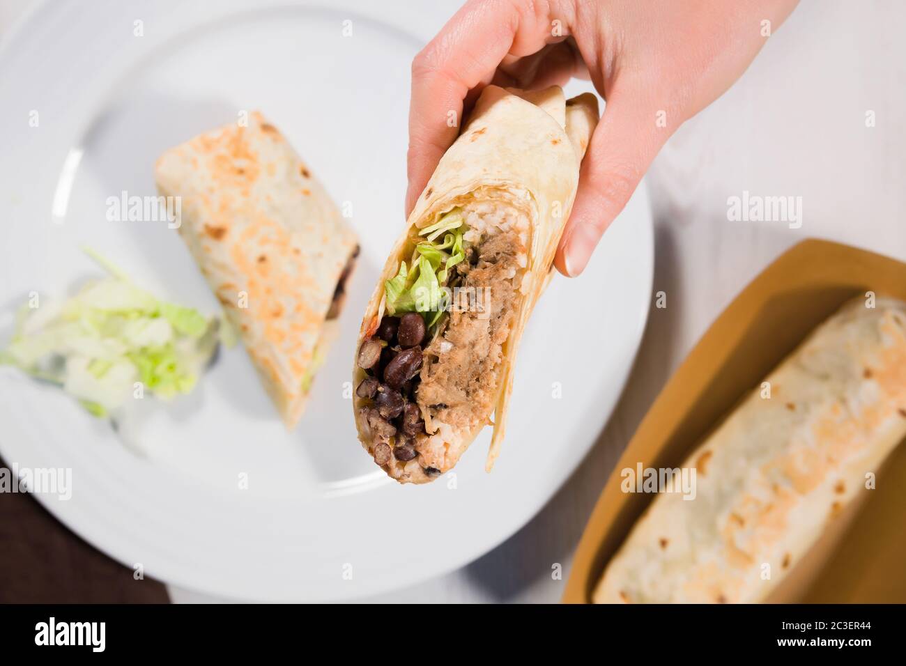 Il burritone avvolge su un piatto bianco con maiale, fagioli, riso e verdure tirate. Foto Stock