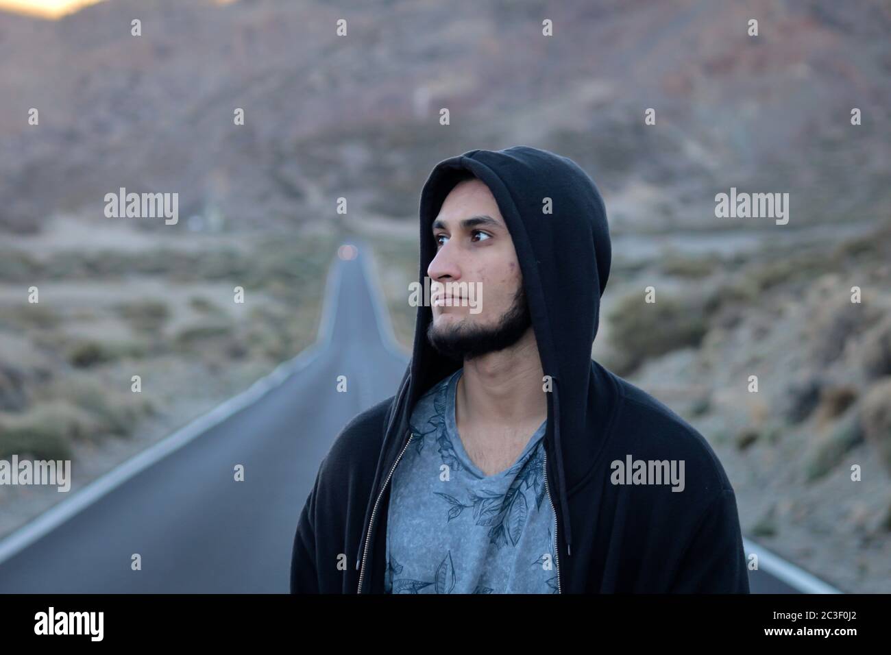 Tenerife, Spagna - 12/19/17: Uomo con la bearded che indossa una felpa nera e guarda in lontananza su una lunga strada diritta Foto Stock